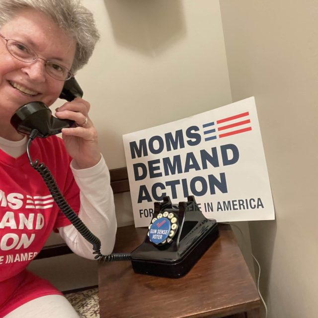Volunteer Michele Mueller smiles while pretending to make a call on a rotary phone.
