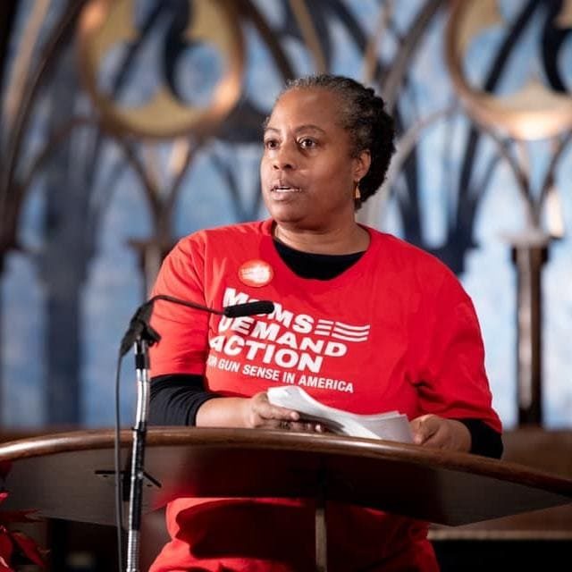 Marie Delus wears a Moms Demand Action shirt while speaking at the podium at an event