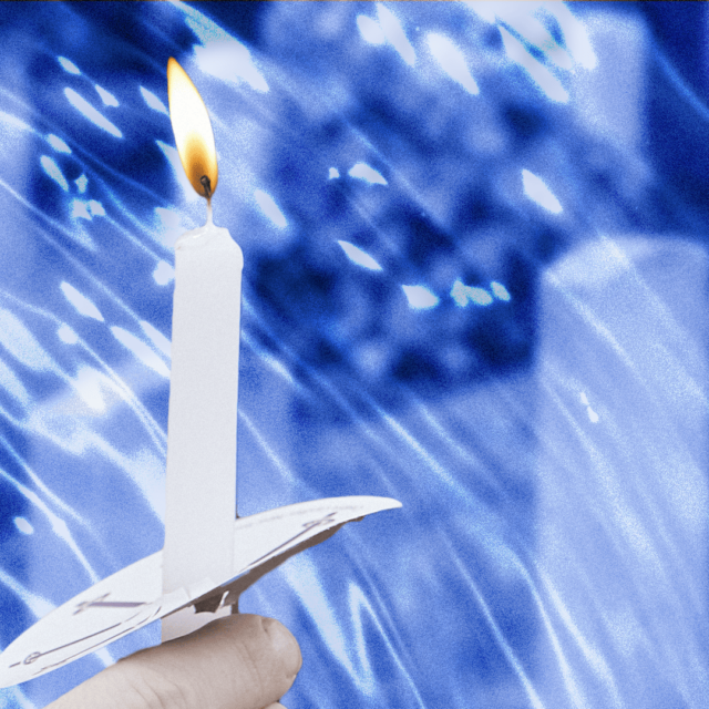 A hand holding a lit candle with tombstones in the background