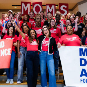 A large group of Moms Demand Action volunteers stand on stairs and cheer. Angela Ferrell-Zabala, executive director of Moms Demand Action, is pictured front and center.